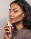 The model wearing Woman holding a gold and white skincare ultrasonic brush against her face.